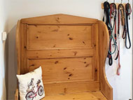 Pine storage seat at end of corridor with hooks for multiple leads, cushion with dog motif and sign above about dogs