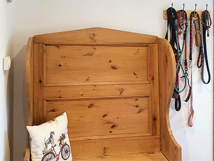 Pine storage seat at end of corridor with hooks for multiple leads, cushion with dog motif and sign above about dogs